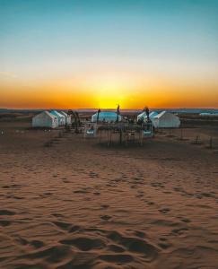 - un coucher de soleil sur une plage avec des tables et des cabanes dans l'établissement Desert Queen Camp ( typical luxury), à Merzouga