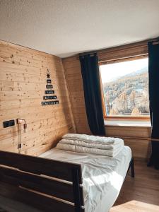 1 dormitorio con 1 cama con pared de madera y ventana en LA FOUX D'ALLOS Centre station, vue panoramique Quartier les étoiles 50m des remontées en Allos