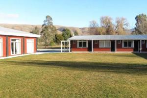 a red house with a large yard in front of it at Home Away from Home - Waitaki Lakes Apartment A5 in Otematata