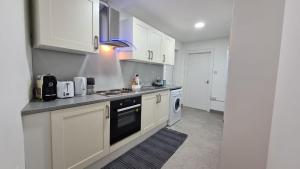 Luxury 1 bedroom flat in the heart of Wood Green في لندن: مطبخ بدولاب بيضاء وفرن علوي موقد