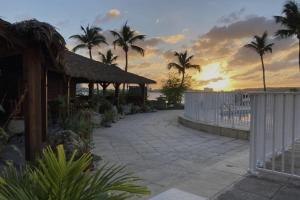 a sunset over a patio with palm trees and a fence at Appartement spacieux au village du flamboyant in Baie Nettle