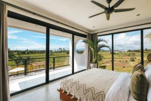 a bedroom with a bed and large windows at Botanique Villa & Studio in Tanah Lot