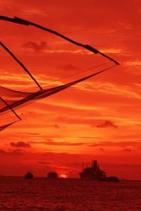 una puesta de sol sobre el océano con un barco en la distancia en Sajhome Fortkochi, Kochi, Kerala, inda en Kochi