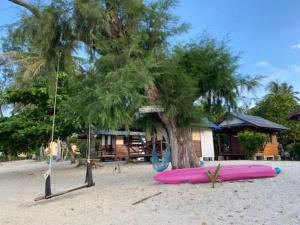 a pink surfboard on the beach next to a tree at Pinks Bungalow in Baan Tai