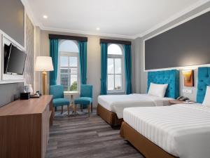 a hotel room with two beds and a desk at Luminor Hotel Palembang by WH in Palembang