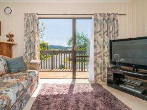 een woonkamer met een bank, een televisie en een balkon bij Jacaranda Lodge - Whangamata Upstairs Unit in Whangamata