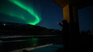 a person standing under a building pointing at the northern lights at Sorrisniva Arctic Wilderness Lodge in Alta