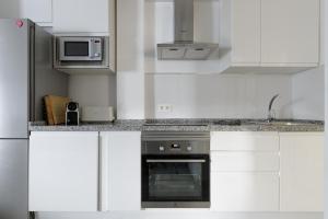 a kitchen with white cabinets and a stove and microwave at Caleta Homes - Apartamentos Pompidou in M&aacute;laga