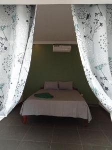 Cama pequeña en habitación verde con cortinas en Little Escape Guesthouse Nesat, en Phumĭ Chroŭy Svay