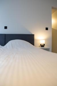 een groot wit bed in een slaapkamer met een lamp bij Hotel Swaenenburg in Oostrozebeke