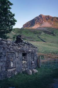 un antiguo edificio de piedra en un campo con una montaña en Welsh holiday home sleeps 5 close to beaches & mountains en Nantlle