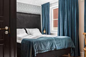 a bedroom with a bed with blue curtains and a window at Donners Hotell in Visby