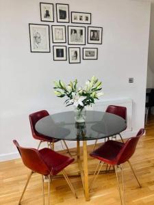 a glass table with red chairs and a vase with flowers at Lovely 2-bed flat with well equipped kitchen in Ealing