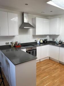 cocina con armarios blancos y encimera negra en Lovely 2-bed flat with well equipped kitchen, en Ealing