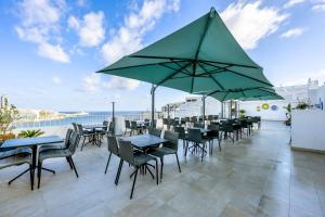 a patio with tables and chairs and a large green umbrella at Plaza Regency Hotels in Sliema