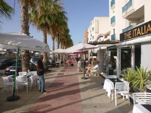 a man standing on a sidewalk with chairs and tables and umbrellas at Kalle Blanca - Cabo Roig in Cabo Roig