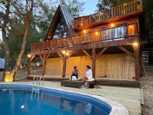 una coppia seduta di fronte a una casa con piscina di Panurla Wooden House havuz & sauna kırmızı a Urla
