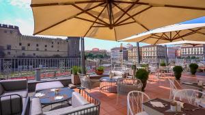 un patio avec des tables, des chaises et des parasols dans l'établissement Mercure Napoli Centro Angioino, à Naples