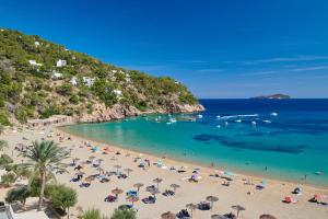 a beach with umbrellas and people in the water at El Somni Ibiza Dream Hotel by Grupotel in Sant Joan de Labritja