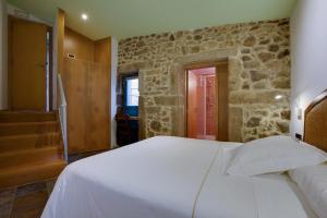 a bedroom with a white bed and a stone wall at Budiño de Serraseca in Oia