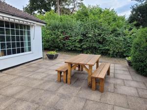 een houten picknicktafel en banken op een patio bij Stunning 2 bedroom cottage on the River Wensum in Earlham