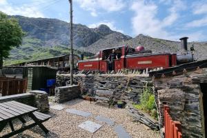 a red train on the tracks with mountains in the background at Traditional 19th Century Slate Miners Cottage in Blaenau-Ffestiniog
