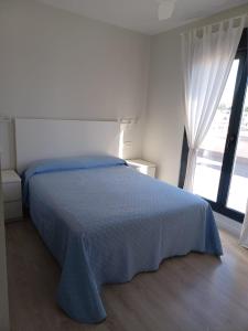 sypialnia z niebieskim łóżkiem i oknem w obiekcie Atico Costa Doñana w mieście Sanlúcar de Barrameda