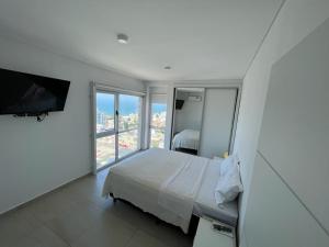 a white bedroom with a bed and a large window at Moderno Depto con Vista al Mar in Comodoro Rivadavia