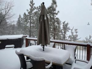 a snow covered table with an umbrella on a deck at CUSTOM SINGLE STORY CABIN WITH JACUZZI POOL TABLE & BIG GAME ROOM WITH ARCADE games in Big Bear Lake