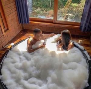 a man and a woman sitting in a bathtub filled with clouds at Chalés Aguá Cristalina in Visconde De Maua