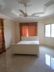 ein weißes Bett in einem Zimmer mit einem Deckenventilator in der Unterkunft Touray Guest House in Old Yundum