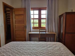 a bedroom with a bed and a desk and a window at Chalé das Palmeiras in Carrancas