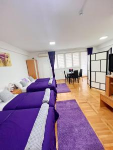 a room with three beds with purple sheets and a table at Apartman Lavanda Banja Koviljaca in Banja Koviljača