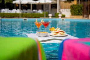 a table with two drinks and food next to a pool at Hotel Villa Romana in Porto Empedocle