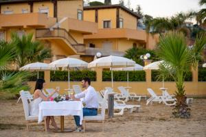 a man and woman sitting at a table on the beach at Hotel Villa Romana in Porto Empedocle