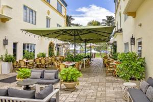 eine Terrasse mit Tischen und Stühlen und einem großen grünen Sonnenschirm in der Unterkunft Hotel Ocean in Miami Beach
