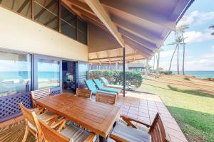 un patio con mesa de madera, sillas y el océano en Kepuhi Beach Cottage 2B, en Maunaloa