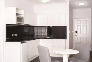 a kitchen with white cabinets and a white table and chairs at Adina Apartment Hotel Brisbane Anzac Square in Brisbane