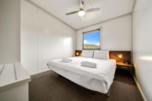 a white bedroom with a large bed and a window at Ecocrackenback 16 Sustainable chalet close to the slopes in Crackenback