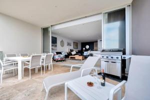 una sala de estar con mesas y sillas blancas y una cocina. en Paradise Penthouse - Beach Front Style and Luxury, en The Entrance