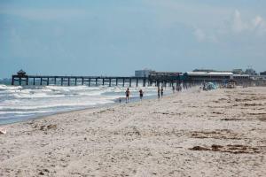 a group of people walking on a beach with a pier at Tahitian Cottage - Heated Pool Walk to the Beach in Cocoa Beach