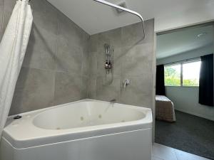 La salle de bains est pourvue d'une baignoire blanche et d'une fenêtre. dans l'établissement Baycourt Lakefront Motel, à Taupo