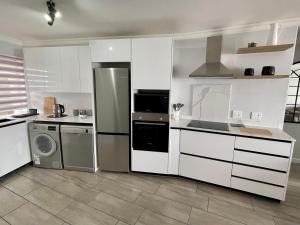 cocina con armarios blancos, lavadora y secadora en Luxurious 2-bedroom beach apartment with a view! en Bloubergstrand