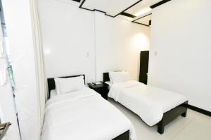 2 camas en una habitación con sábanas y almohadas blancas en Swiftlets Inn en El Nido