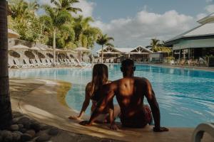 un hombre y una mujer sentados en una tabla de surf junto a una piscina en Résidence l'Archipel, en Saint-Gilles-les-Bains