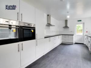 a white kitchen with white cabinets and black appliances at Kunda House Gillotte in Birmingham