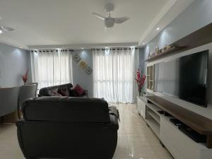 uma sala de estar com uma televisão de ecrã plano e um sofá em Pé na Areia a Poucos Metros -Apartamento Guarujá Pitangueiras no Guarujá