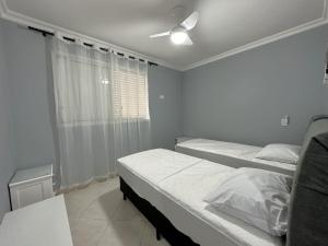 a bedroom with two beds and a ceiling fan at Pé na Areia a Poucos Metros -Apartamento Guarujá Pitangueiras in Guarujá
