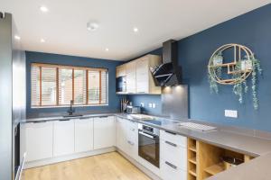 Stylish & modern 4-bedroom home with sea views في برايتون أند هوف: مطبخ فيه دواليب بيضاء وحائط ازرق