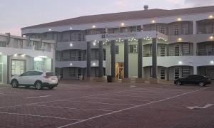un grand bâtiment avec deux voitures garées dans un parking dans l'établissement SHALIMAR GARDENS HOTEL, au Cap